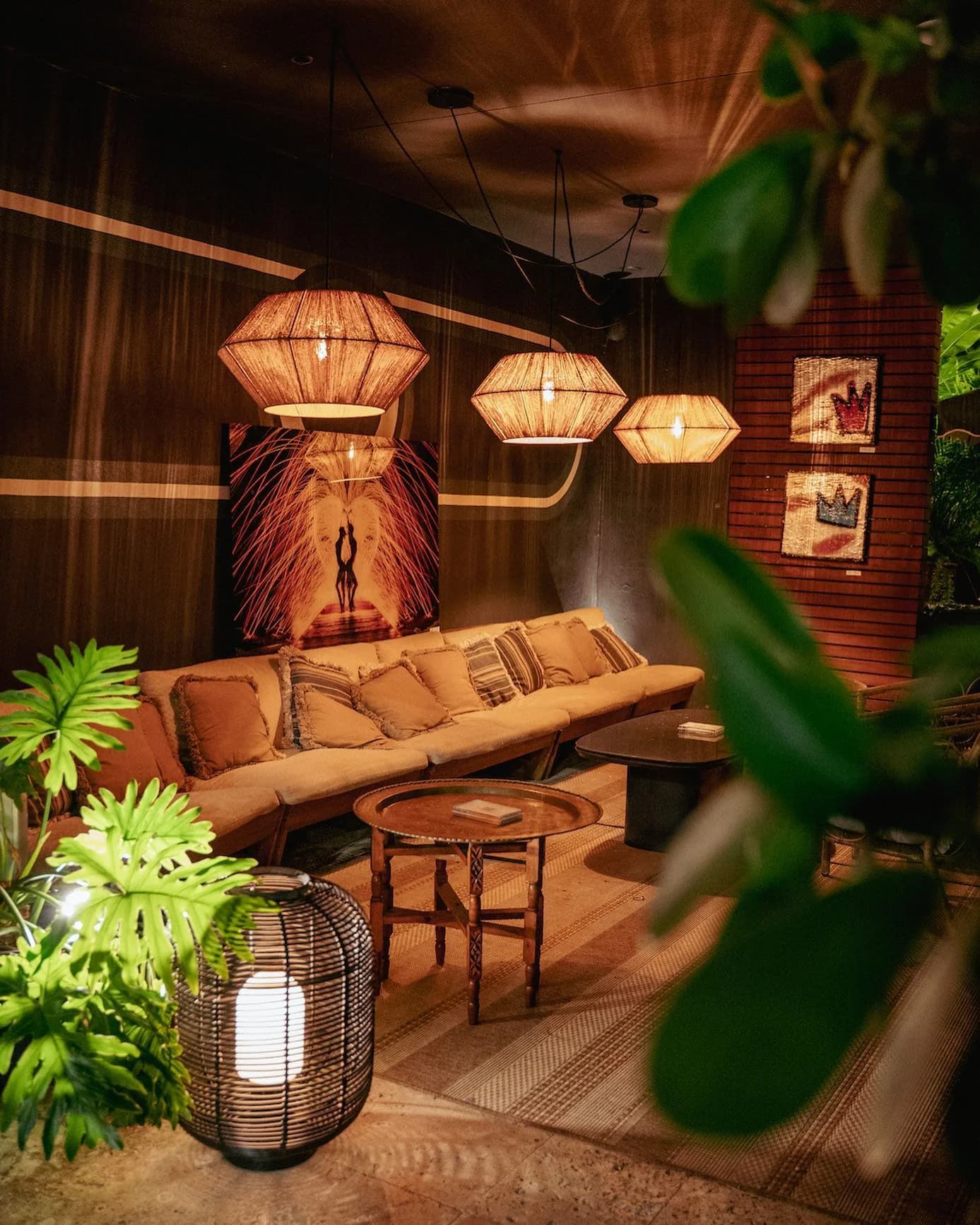 The Layla lounge with woven pendant lights, a sofa and tropical plants.