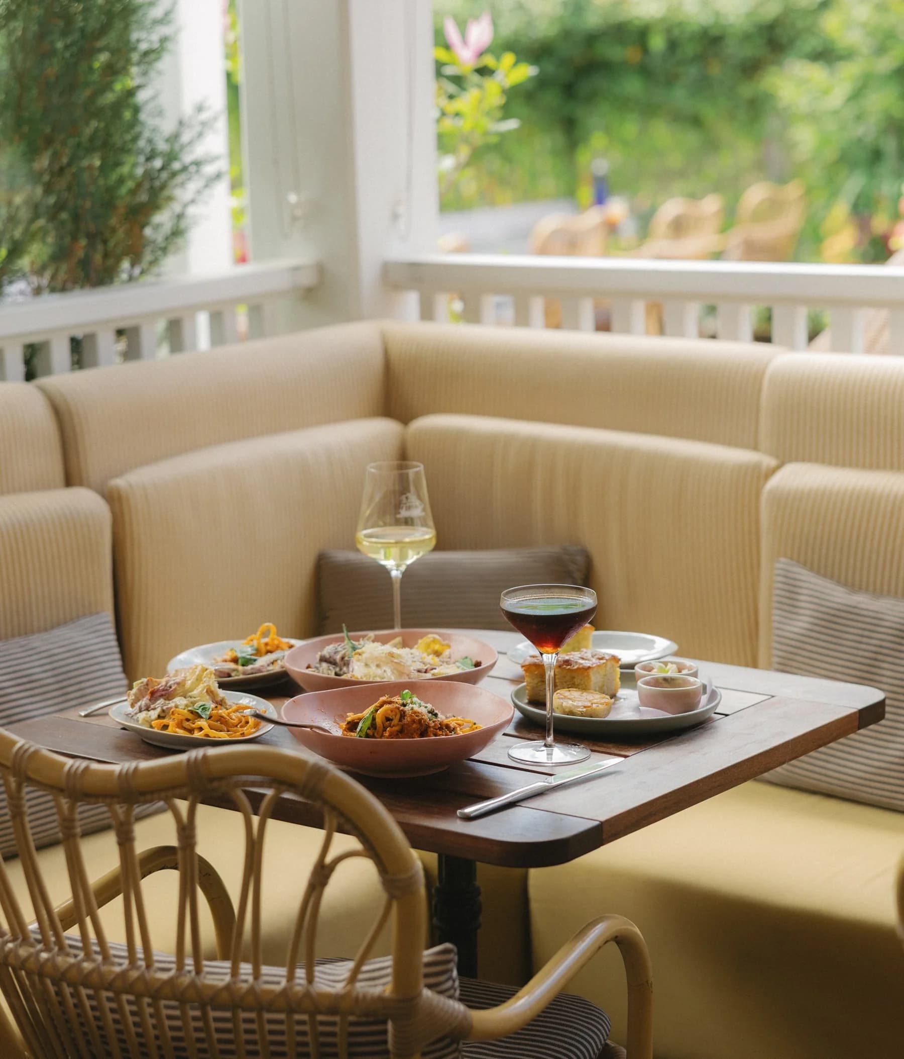 A sunlit table set with dishes and drinks beside cream seating at Sister Ship.
